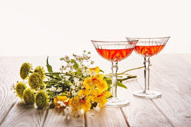 close-up shot of glasses of wine with field flowers bouquet on wooden table on white - Foto, imagen