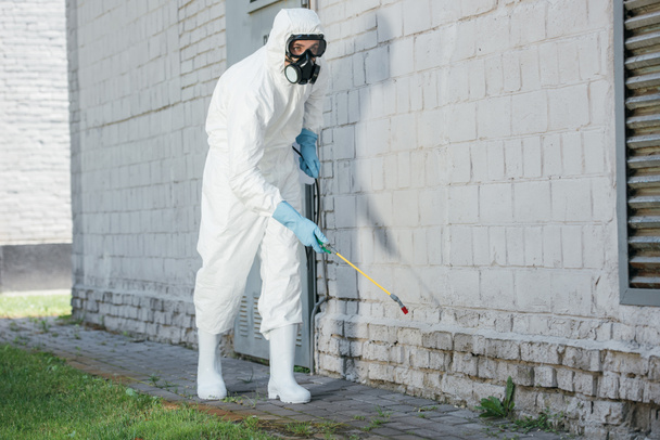 trabajador de control de plagas pulverización de productos químicos con pulverizador en la pared del edificio
 - Foto, Imagen