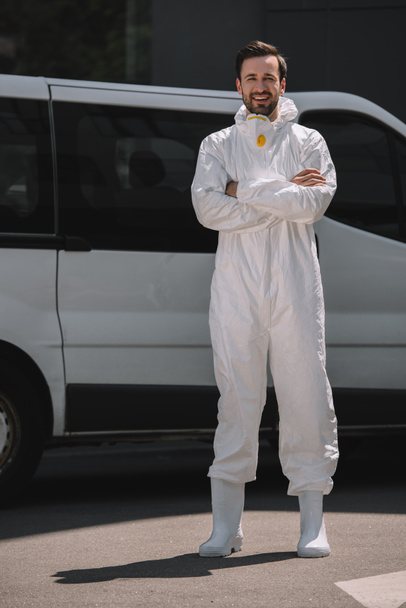 smiling pest control worker with crossed arms looking at camera near car on street  - Photo, Image
