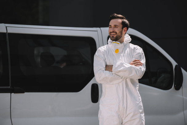 uśmiechający się pracownik kontroli szkodników w jednolite stojący z skrzyżowanymi rękami w pobliżu samochodu na ulicy  - Zdjęcie, obraz