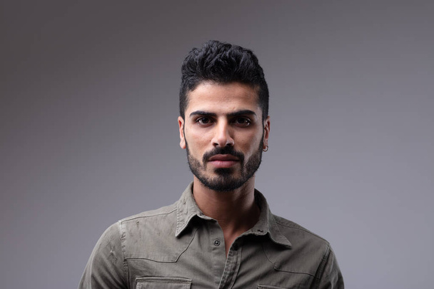 Single dark skinned young man with well groomed beard wearing stylish grey button shirt and serious expression - Foto, Imagen