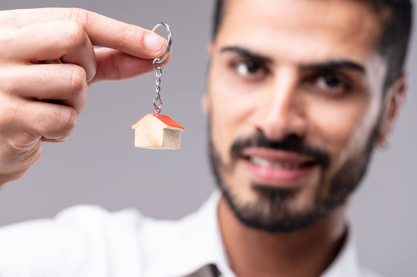 Усміхнений чоловік тримає ключове кільце з мініатюрним будинком в концепції будинку мрії, власності, купівлі або продажу або нерухомості з фокусом на руці
 - Фото, зображення