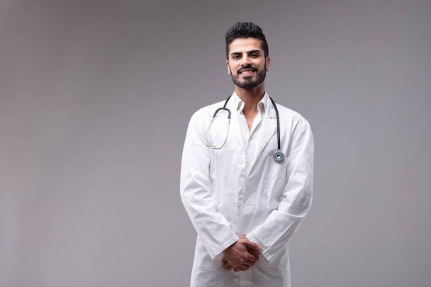 Porträt eines jungen, gut gelaunten, bärtigen Arztes im weißen Kleid - Foto, Bild