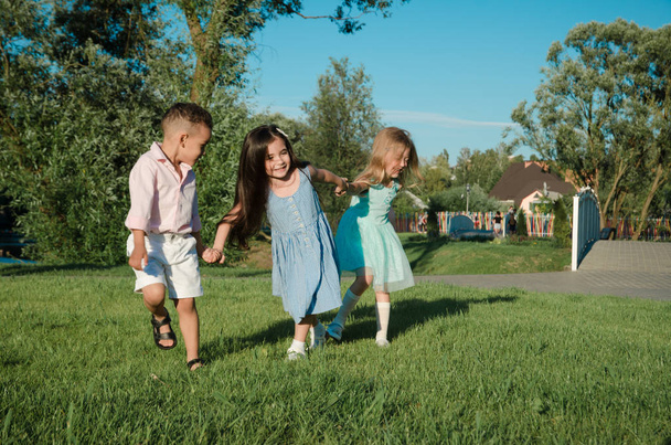 Маленькие дети играют на лужайке. две девочки и мальчик
 - Фото, изображение