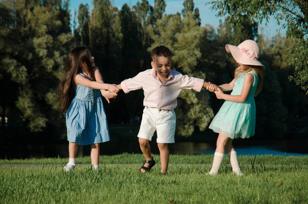 małe dzieci, zabawy na trawniku. dwie dziewczyny i chłopak - Zdjęcie, obraz
