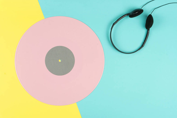 top view of a pink long play vinyl record or LP with a black on-ear headphone on the yellow and blue background - Fotó, kép