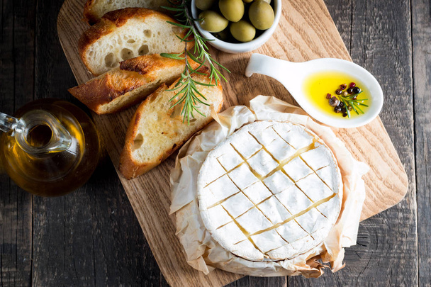 Baked camembert cheese. Fresh Brie cheese and a slice on a wooden board with nuts, honey, rosemary, baguette bread grilled toasts and leaves. Brie type of cheese. Italian, French cheese. - Zdjęcie, obraz