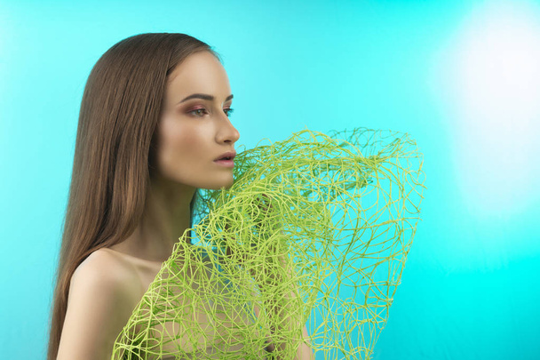 Beautiful naked shoulders young girl wearing green grass type veil mesh on her face covers her breast and face. Isolated on blue. Healthy skin. Copy space. Advertising and conceptual design. - Fotografie, Obrázek