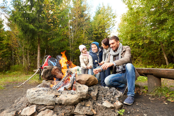 happy family roasting marshmallow over campfire - Foto, Imagen