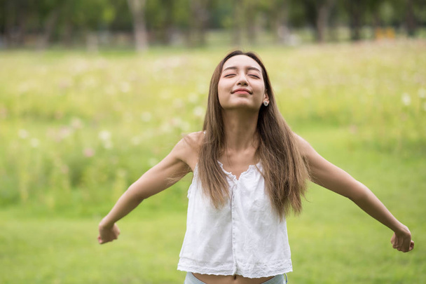 Gyönyörű ázsiai nő portréja belélegezni a friss levegőt a zöld nyári park állva, csukott szemmel és kinyújtott karok - Fotó, kép