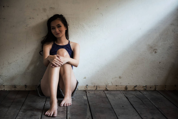 Портрет психической болезни Азиатская красивая женщина сидит на деревянном полу в пустой комнате с легким оттенком у окна
. - Фото, изображение