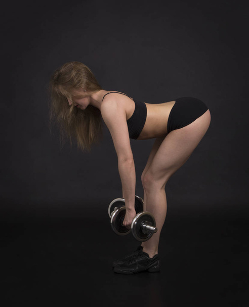A young woman engaged in fitness with dumbbells. Studio shot on black background. Isolated image. - Φωτογραφία, εικόνα