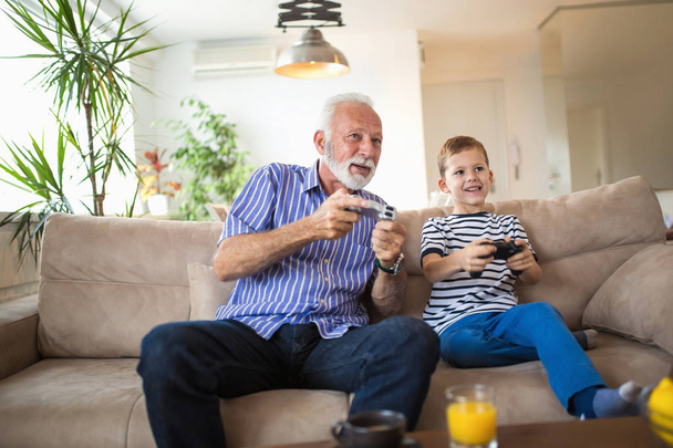 Isoisä ja pojanpoika pelaavat videopelejä kotona
 - Valokuva, kuva