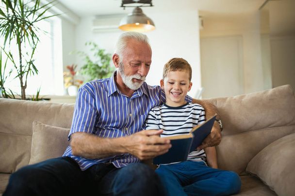 Grandfather with grandson reading together on sofa - Photo, Image