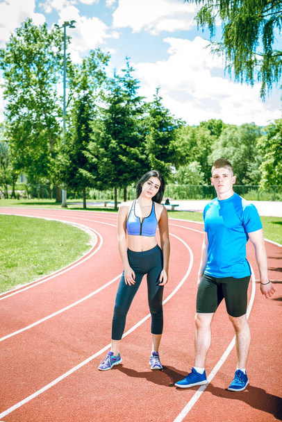 Young adult couple standing and talking on athletics track field during hot sunny summer day. Toned image. - Photo, Image