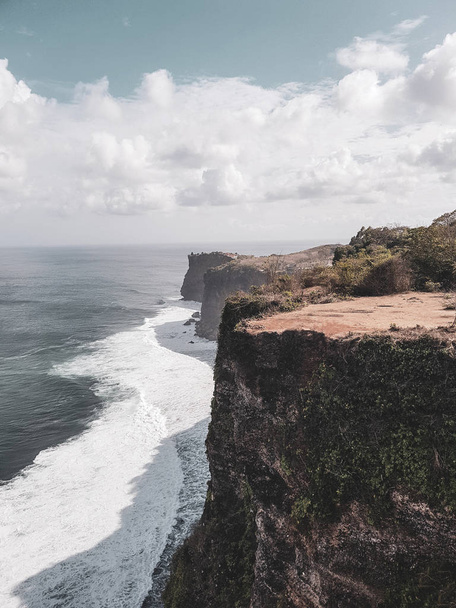 Beautiful Uluwatu cliffs in Bali over ocean and cloudy sky background, Indonesia - 写真・画像