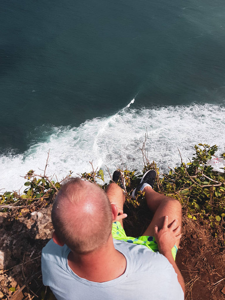 Vista superior del joven turista sentado en el acantilado con increíble vista al mar
 - Foto, Imagen