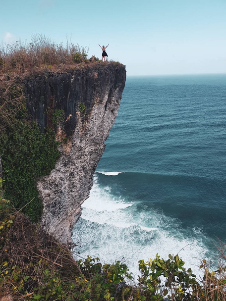 Дівчина стоїть з піднятими руками на скелі з дивовижним океаном і хмарним видом на небо
 - Фото, зображення