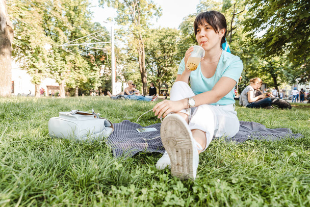 都市公園で冷たい飲み物を保持している女性。背景をぼかし。広角 - 写真・画像