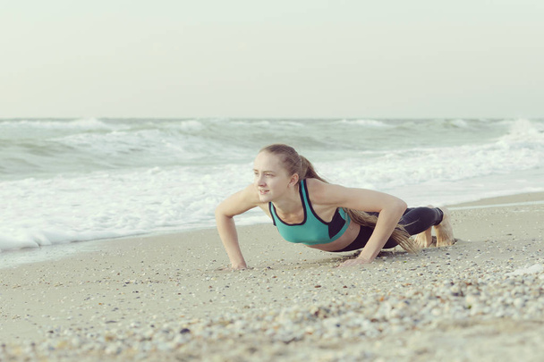 Girl push-ups on the beach, waves in the background - Foto, afbeelding