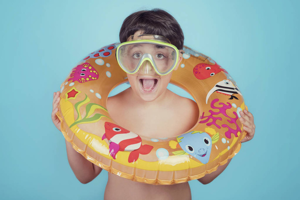 gelukkig kind lacht met float ring op blauwe achtergrond - Foto, afbeelding