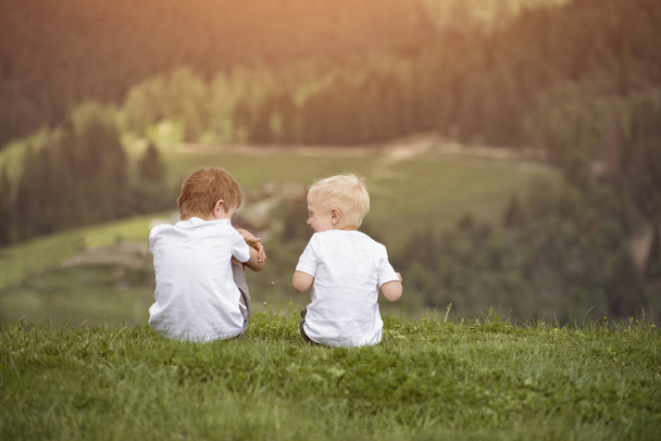 Два мальчика сидят на холме и веселятся. Вид сзади
 - Фото, изображение