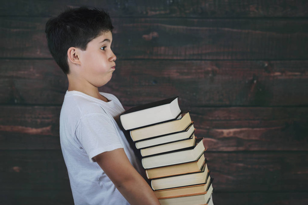 niño con pila de libros sobre fondo de madera
 - Foto, imagen