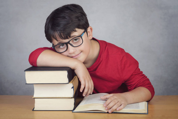 garotinho sorridente apoiando-se em livros em uma mesa
  - Foto, Imagem