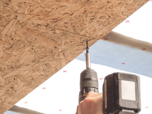 строитель вкручивает винт в лист OSB на потолке
 - Фото, изображение