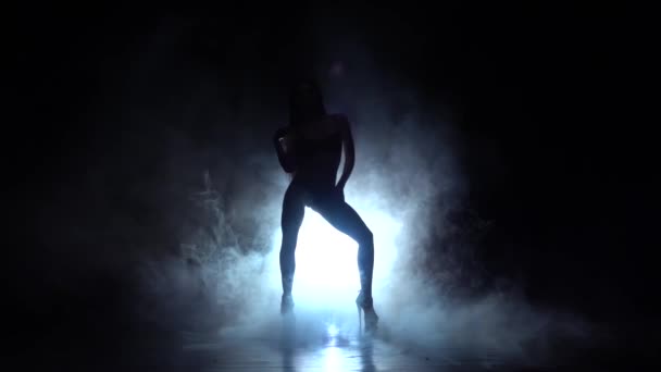 Dívka tančí sexy tanec na vysokých podpatcích. Na pozadí černého kouře. Silueta. Zpomalený pohyb - Záběry, video