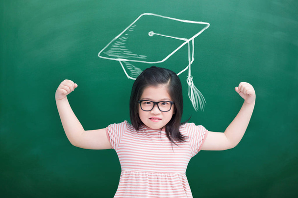 cute girl showing  strong arms with bachelor cap on green chalkboard - Φωτογραφία, εικόνα