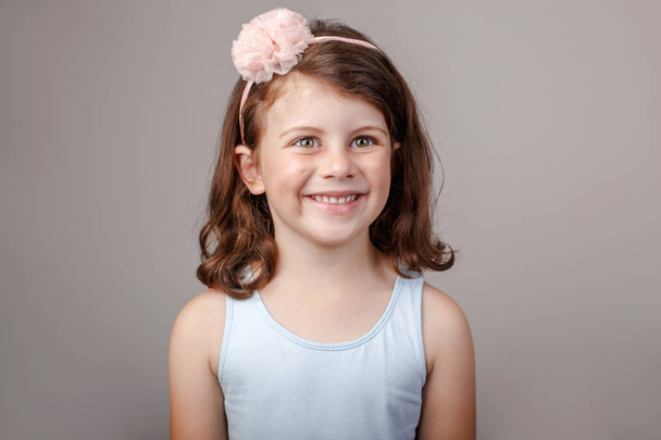 Closeup portrait of cute adorable white brunette Caucasian preschool girl making faces in front of camera. Child smiling laughing posing in studio on plain light background. Kid expressing emotions - Photo, Image
