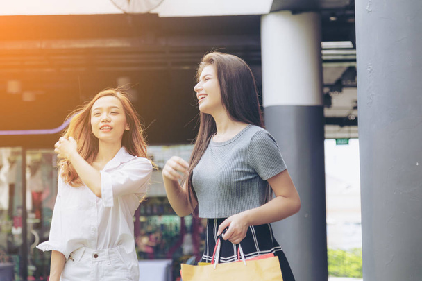 Asya kız ve arkadaşı etnik Alman-Tay alışverişe çanta ve akıllı telefon alışveriş merkezinde tutarak. Yumuşak flare filtre. - Fotoğraf, Görsel