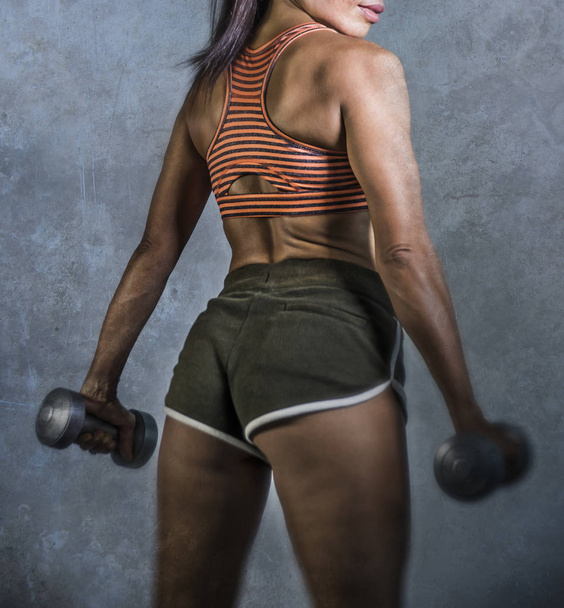grunge sport advertising style portrait of young athletic woman with strong back and fit body holding dumbbells in fitness training workout isolated on grunge background in healthy lifestyle  - Photo, Image
