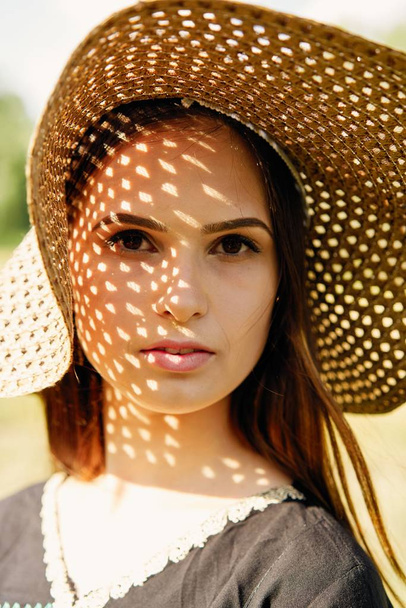 Beautiful young woman in straw hat posing outdoors at sunny summer day  - Foto, afbeelding
