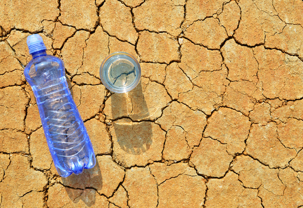 Pullo ja lasi vettä kuivalla säröillä maaperään. Ilmaston lämpenemisen käsite
. - Valokuva, kuva