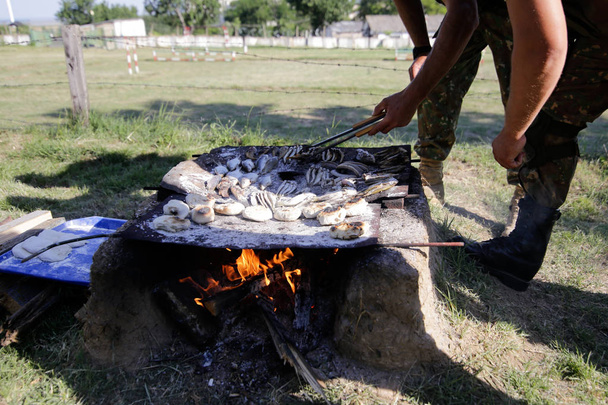 Vojáci připravují jídlo na ručně vyráběné grilu na dřevěné krbem, na táboře přežití. Vaří, vodních hadů, ryb, žab a chléb. - Fotografie, Obrázek
