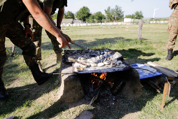 Soldaten bereiden van de maaltijd op een handgemaakte grill op houten openhaard, in een survival kamp. Ze koken water slangen, vissen, kikkers en brood. - Foto, afbeelding