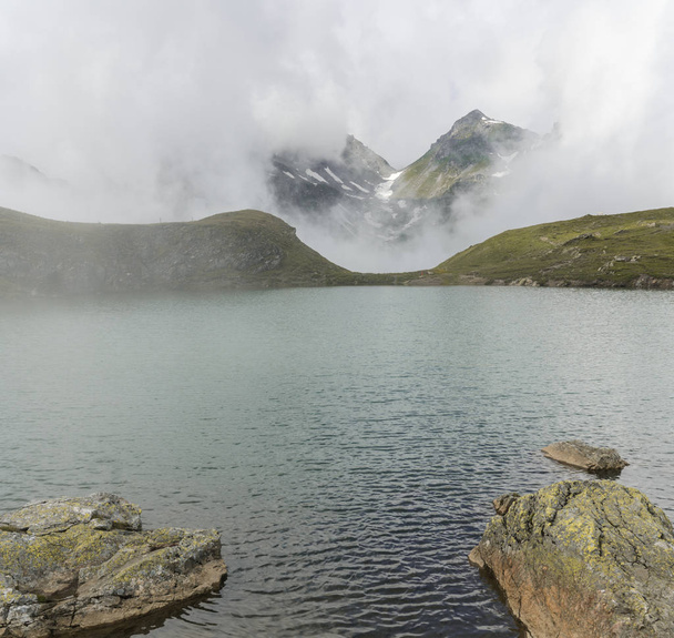 idyllic mountain lake with fog lifting to reveal high alpine mountains - Fotó, kép