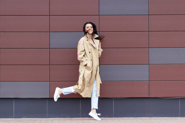 Mooie vrouw in de beige jas en jeans op de achtergrond van de straat, zachte focus - Foto, afbeelding
