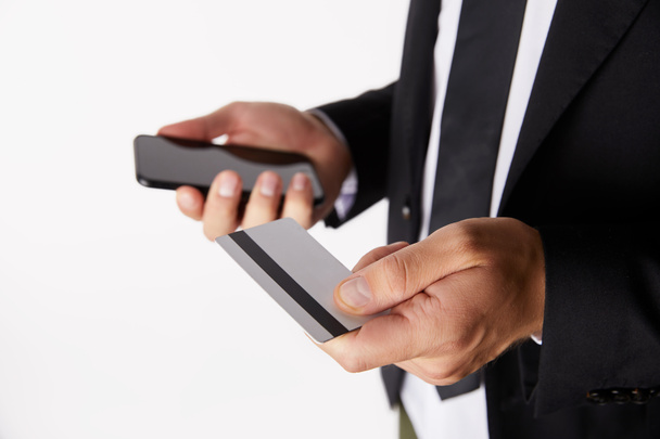 imagen recortada de hombre de negocios haciendo compras en línea con tarjeta de crédito y smarpthone aislado sobre fondo blanco
  - Foto, Imagen