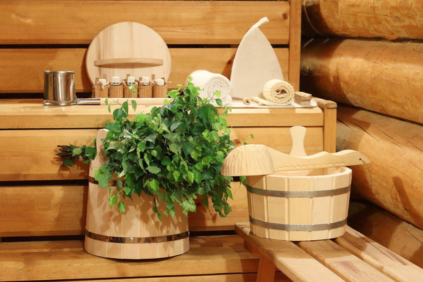 Vassoura de bétula fresca no balde de madeira e acessórios de banho na sauna
. - Foto, Imagem