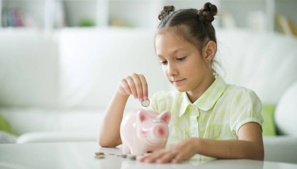 Cute little girl with a piggy bank at home - 写真・画像