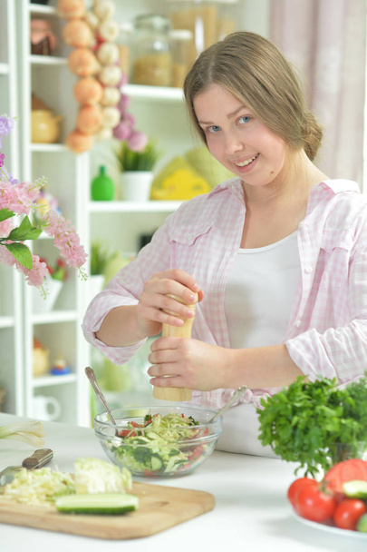 Cute teen girl preparing fresh salad on kitchen table   - Foto, Bild