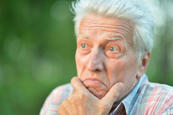 portrait d'un homme âgé réfléchi avec la main sur le menton dans le parc
 - Photo, image
