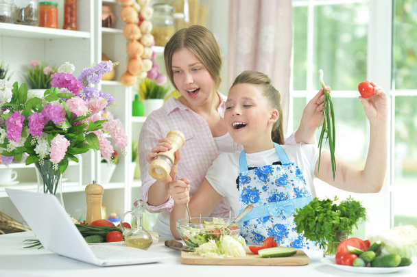 Two funny girls preparing fresh salad on kitchen table   - Foto, Imagem