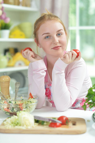 Cute teen girl preparing fresh salad on kitchen table   - Фото, изображение