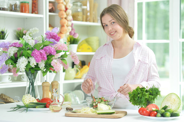 Cute teen girl preparing fresh salad on kitchen table   - Fotoğraf, Görsel