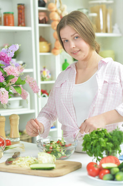 Cute teen girl preparing fresh salad on kitchen table   - Φωτογραφία, εικόνα