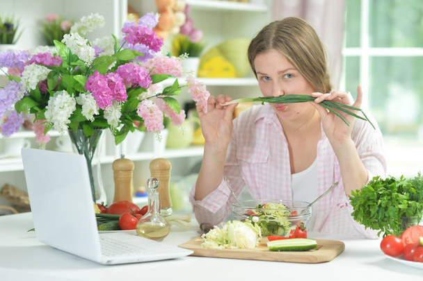 Cute teen girl having fun while cooking salad on kitchen table   - Фото, изображение